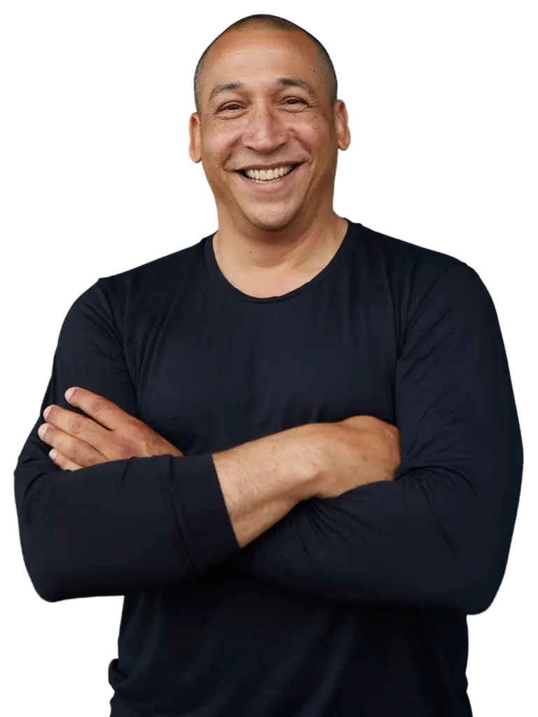Pictured is Juan Conde, a man of Puerto Rican descent wearing a black long-sleeved shirt with his arms crossed and a smile.